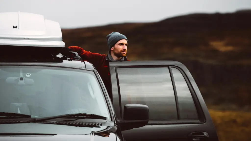 man standing next to the open door of an SUV with  roof racks and a roof top box